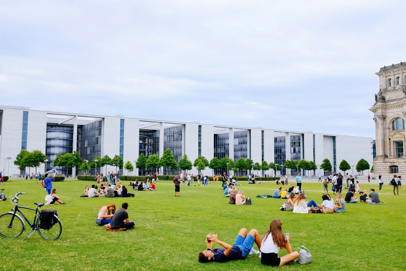 Students sit and lie on a wide sunny lawn in front of a long modern campus building